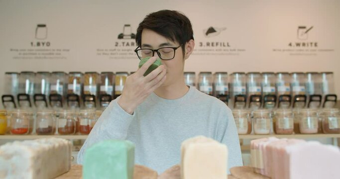 Man buying eco bio organic goods products in zero waste shop. Asian male holding a bar of ecological handmade soap in plastic free grocery store. Natural cosmetics, skin care. Sustainable lifestyle.
