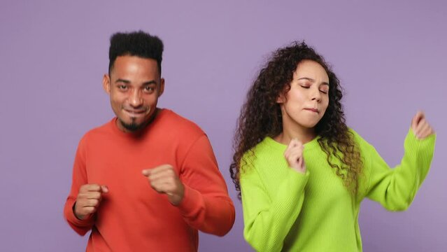 Young couple two friends family man woman of African American ethnicity wear casual clothes together dance clench fists gesticulating hands fooling around have fun isolated on plain purple background