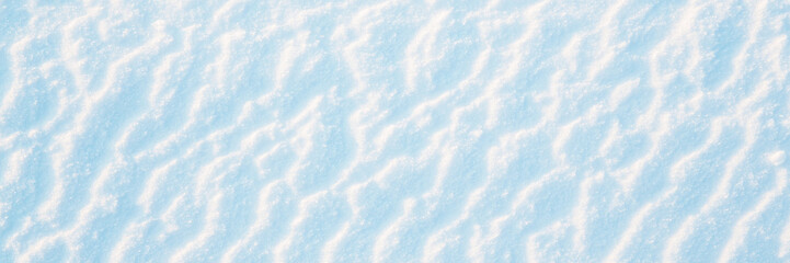 Obraz premium Wide panoramic winter background with snowy ground. Natural snow texture. Wind sculpted patterns on snow surface.