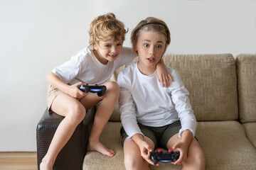 Cute children joyful playing video games with controller console, brother sister expressing emotions while enjoying their hobby playstation joystick.