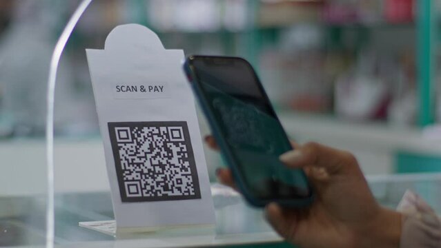 A close-up shot of a hand of a customer scanning a barcode to pay e-money to an electronic bank account or online UPI transfer in a general or grocery store with a shopkeeper in the background.