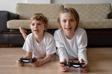 Fototapeta premium Cute children joyful playing video games with controller console, brother sister expressing emotions while enjoying their hobby playstation joystick.