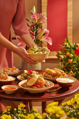 Tet banquet with a hand model holding a bowl of soup. Flowers and Kumquat tree as the background. for holiday food advertising. Young women wearing Vietnamese traditional costumes and traditional food
