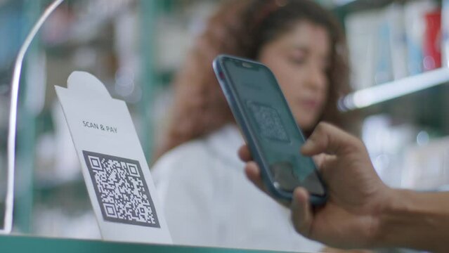 A close-up shot of a hand of a customer scanning a barcode to pay e-money to an electronic bank account or online UPI transfer in a medical store or pharmacy with a smiling woman in the background