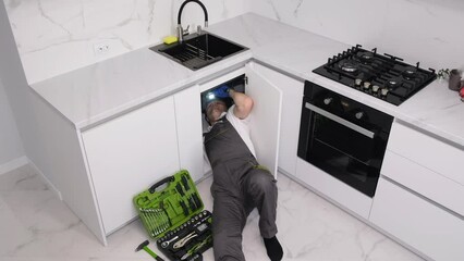 A male plumber is fixing a sink for washing dishes for an advertisement for plumbing services