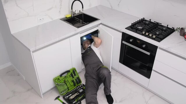 A male plumber is fixing a sink for washing dishes for an advertisement for plumbing services