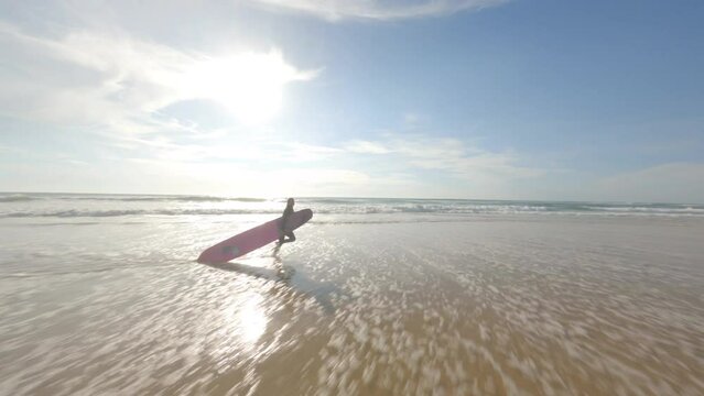 Surfer with surfboard running along sea shore of deserted beach, Landes in France. Aerial drone fpv