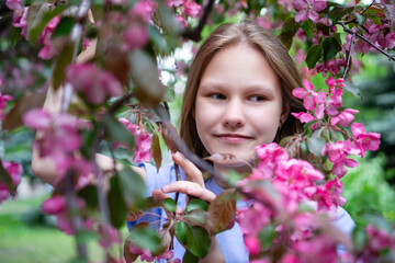 Fototapeta premium Spring face of a girl. Close-up portrait of a tender woman on the background of sakura flowers. Hanami festival in cherry blossom garden. Young blonde woman standing in sakura park. High quality photo
