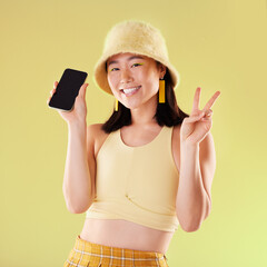 Portrait, peace sign and Asian woman with phone in studio isolated on a yellow background mockup....