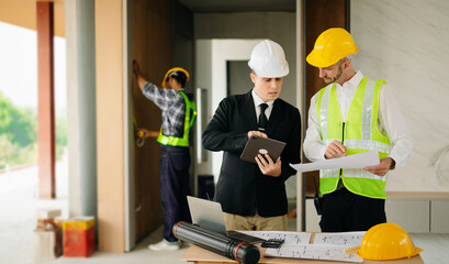 Contractor and architect looking at plan, tablet, laptop and talking about working on big project. Building in construction process.