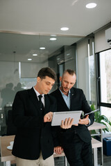 Kind leader executive manager share and discuss business solutions plan ideas on tablet with male marketing manager in modern office..