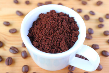 Cup of Ground Coffee on Wooden Table with Scattered Roasted Coffee Beans