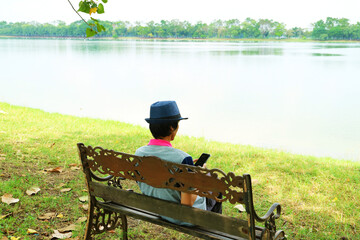Naklejka na ściany i meble Man Sitting on the Lakeshore Bench Checking on His Smartphone