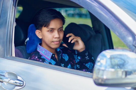 Portrait of smiling handsome young Asian man wearing batik talking on mobile phone and driving in the car. people lifestyle concept