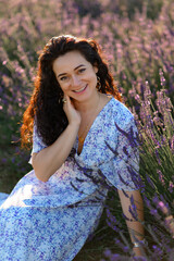 Portrait of a happy woman in a blue dress enjoying a sunny summer day in a lavender field. Fresh air, Lifestyle.