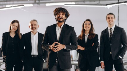 Team leader posing with his colleagues and smiling. Young company CEO standing in front of employees