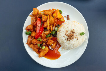 A plate of sweet and sour chicken with boiled rice, a Chinese inspired food served in a UK food court.