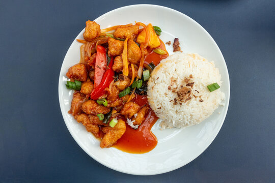A plate of sweet and sour chicken with boiled rice, a Chinese inspired food served in a UK food court.