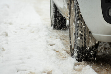 Close up of car wheels starting movement with slip on snowy uncleaned road. Traffic on winter road after heavy snow