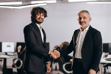 Smiling businessmen shaking hands after business deal. Two entrepreneurs having an agreement. Company coworkers in suits greet each other in office
