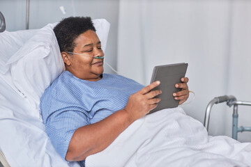 Side view portrait of African American senior woman using digital tablet while laying on bed in...