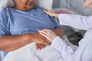 Obraz premium Close up of caring young nurse supporting female patient in hospital bed