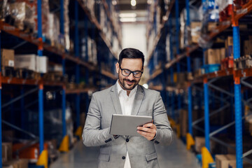 A smiling warehouse supervisor is adding orders on tablet.