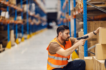 A delivery center worker is loading qr and bar codes while crouching in facility.