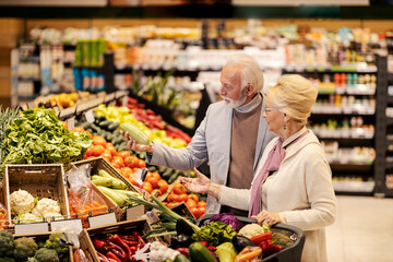 A senior couple is choosing fresh vegetables at the supermarket.