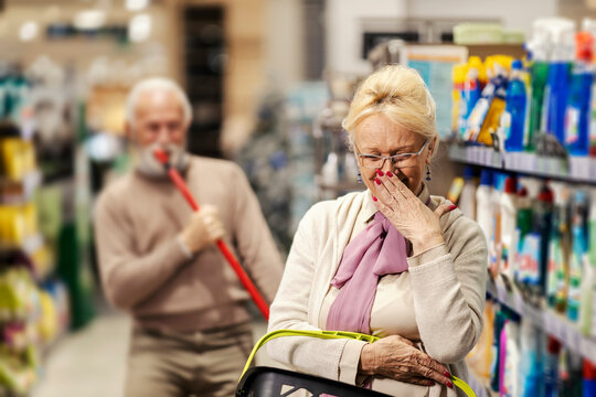 A senior woman is laughing at her husband who is singing and goofing around in supermarket.