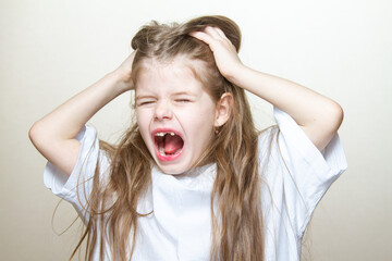 Portrait of a cute little blonde girl showing emotions, screaming and pulling her hair. A young...