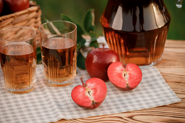 Two glasses with apple juice and basket with apples on wooden table with natural orchard background. Vegetarian fruit composition