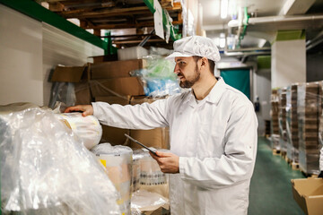 A hardworking food factory worker is working with tablet in storage.