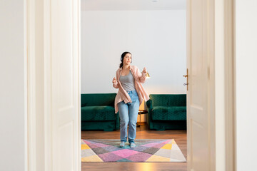 Fototapeta na wymiar Young Caucasian pretty woman wearing headphones dancing in living room. View from white doors. Home recreation