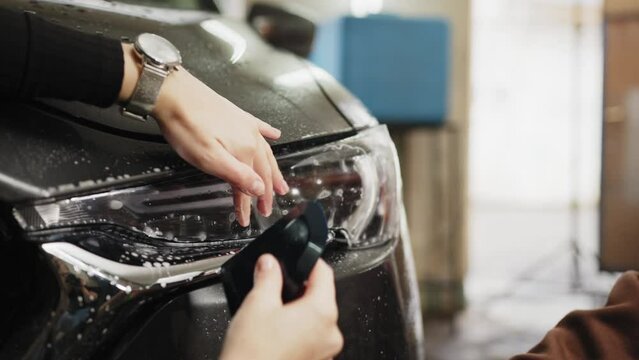Close up of protection film installation on front headlight of modern luxury car. PPF, polyurethane film applied to car surface to protect the paint from stone chips, bug splatter, and abrasion.
