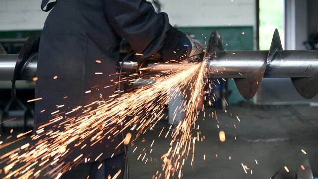 Cutting agricultural equipment. A man grinds a metal structure at a factory.