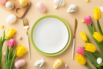 Easter concept. Top view photo of empty plates cutlery colorful easter eggs ceramic bunnies yellow and pink tulips and wooden egg holder on isolated pastel beige background