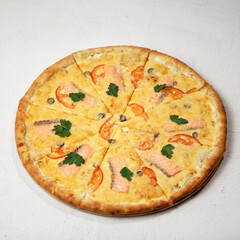 Pizza with cheese, salmon and tomatoes cut into pieces, garnished with parsley. Pizza with seafood. Italian Cuisine. Isolate on white background. View from above. Copy space. 
