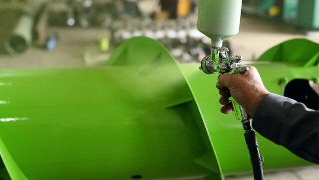 Man spraying green paint on the metal surface of agricultural equipment.