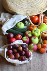 Straw bag and reusable fabric bags filled with various healthy fruit and vegetables. Wooden background, selective focus.