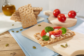 brown crispbreads with tomatoes and cheese on a wooden board. healthy snack with cereal bread. breakfast on a sunny day. crispy bread stuffed with vegetables