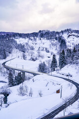雪国の里山に伸びる除雪されたS字カーブの道路