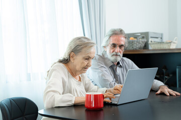 Fototapeta premium Retired old Asian male and his wife hand use Asian senior couple working and check data information with laptop on table in living room at home.