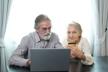 Cheerful mature retired couple shopping on Internet with ecommerce online app on laptop together at home,wireless communication.