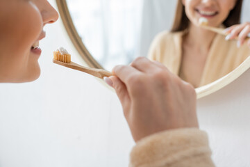 cropped view of young and happy woman brushing teeth near mirror in bathroom.