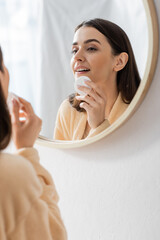 reflection of brunette young woman cleansing face with cotton pad in bathroom mirror.