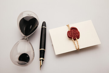 Envelope with wax seal stamp, pen and hourglass on a table