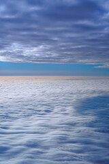 Fototapeta na wymiar A beautiful view over the clouds from the aircraft window. Flying between layers of white clouds overlooking an azure sky and a golden sunlit edge. Vertical photo.