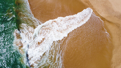 Aerial view of the waves with foam on the sandy ocean shore. Beautiful texture background for tourism and design. Tropical seashore