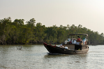 Fototapeta na wymiar 11th February, 2023, Sundarban, West Bengal, India: Few ferry boats carrying daily needs items on the river at Sundarban Tiger reserve, India.